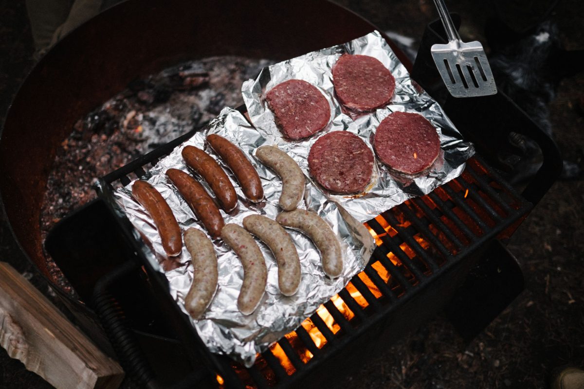 Hamburgers and bratwurst cooking over a campfire