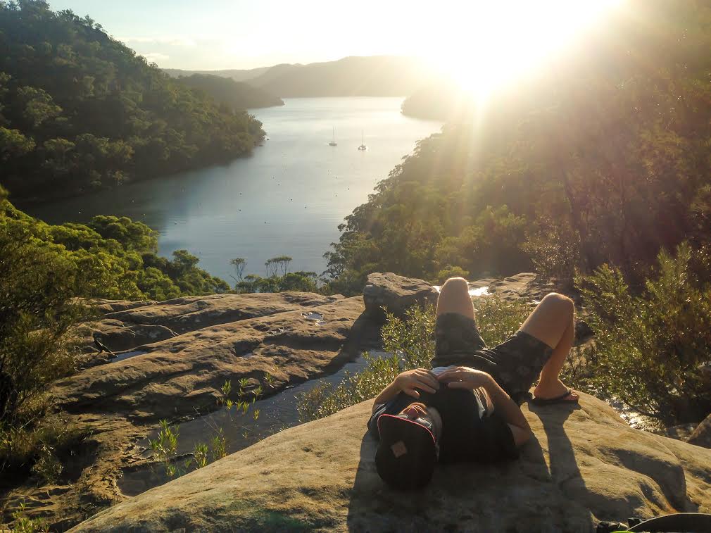 Man laying in the sun on a rock on America Bay walking track, Ku-ring-gai Chase National Park. Photo: Instagram @hiphikers