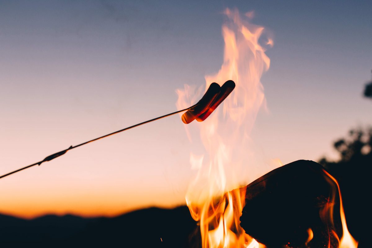 Sausages on stick held over flame. Photo: Unsplash