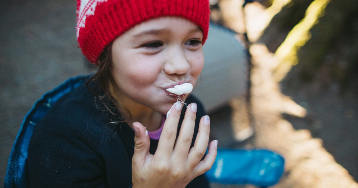 Child eating a marshmallow by a campfire