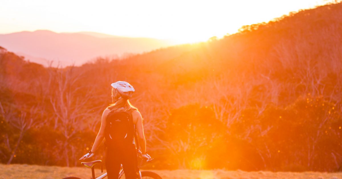 Person standing in the sunset with a mountain bike on the Thredbo Valley track, Kosciuszko National Park. Photo: Boen Ferguson/DPIE