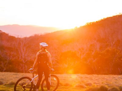 Person standing in the sunset with a mountain bike on the Thredbo Valley track, Kosciuszko National Park. Photo: Boen Ferguson/DPIE