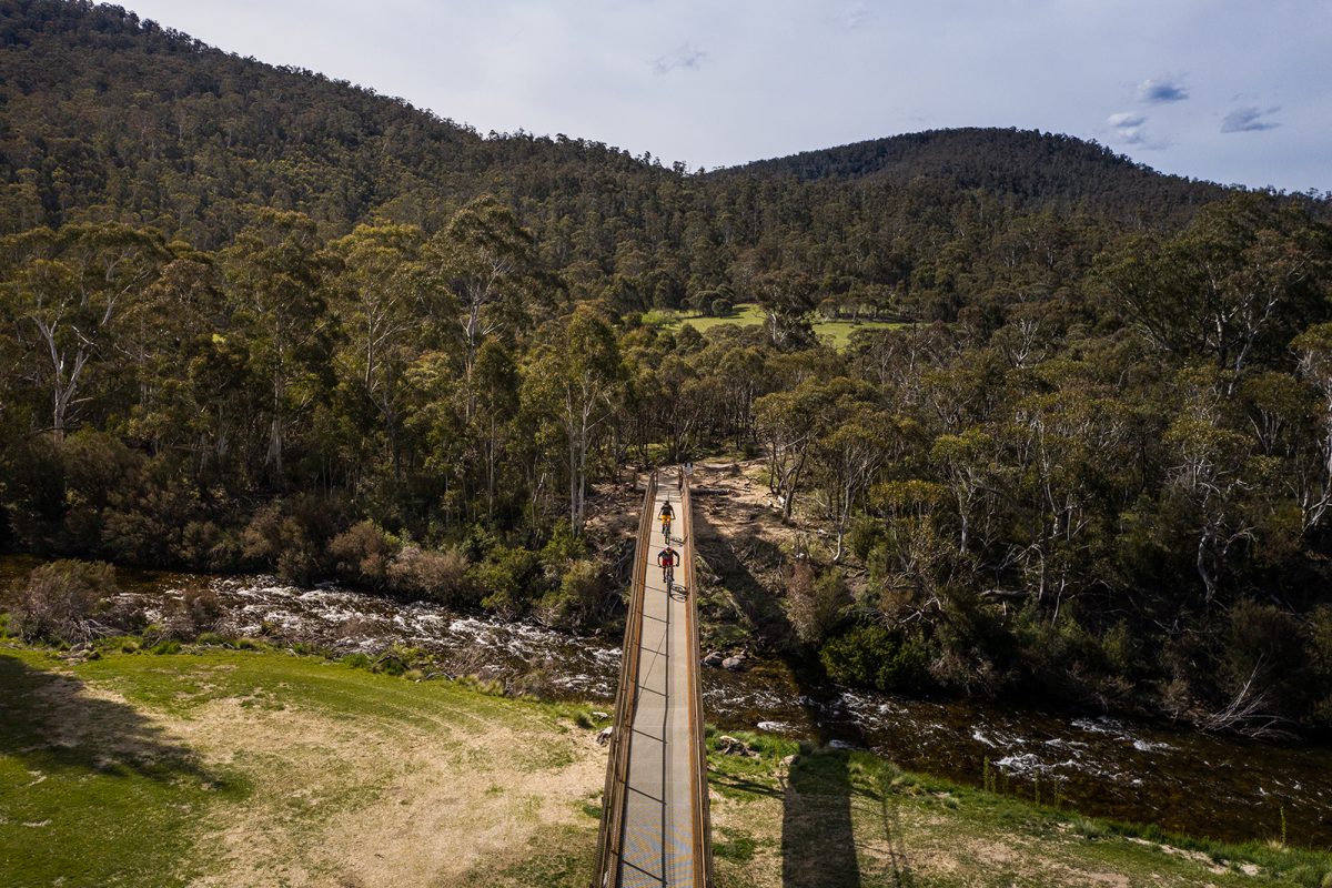 Aerial view of two guys riding the final bridge of the Lower Thredbo Valley track, Thredbo-Perisher area in Kosciuszko National Park. Photo: Rob Mulally/DPIE
