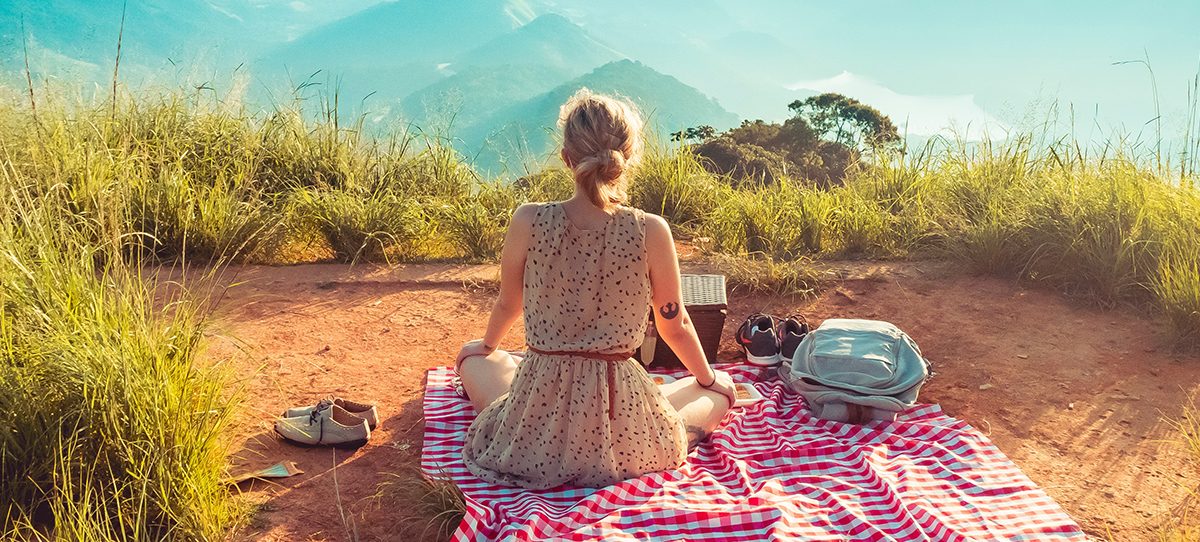 Woman sitting on a picnic blanket with a mountain view in front of her. Photo: William Justen De Vasconcellos