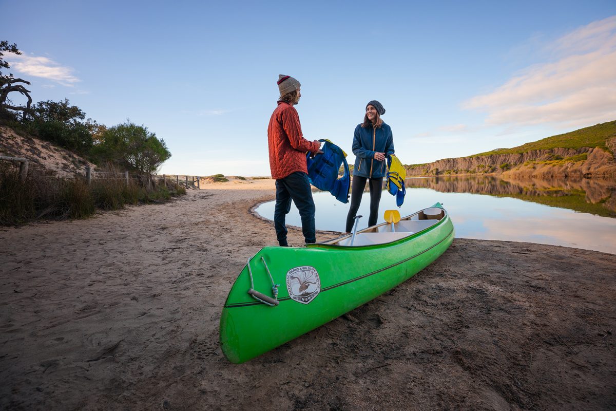 A couple putting life jackets on to go canoeing in the lagoon in Bournda National Park. Photo: Daniel Tran/DPIE