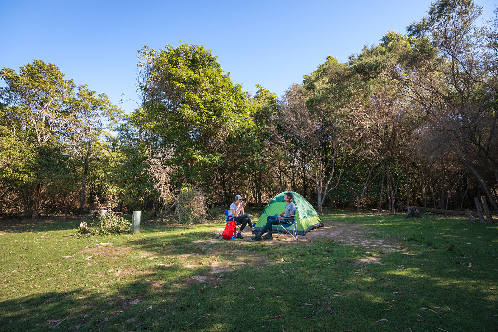 A couple sitting in camp chairs in front of their tent in Hobart Beach campground, Bournda National Park. Photo credit: Daniel Tran/DPIE