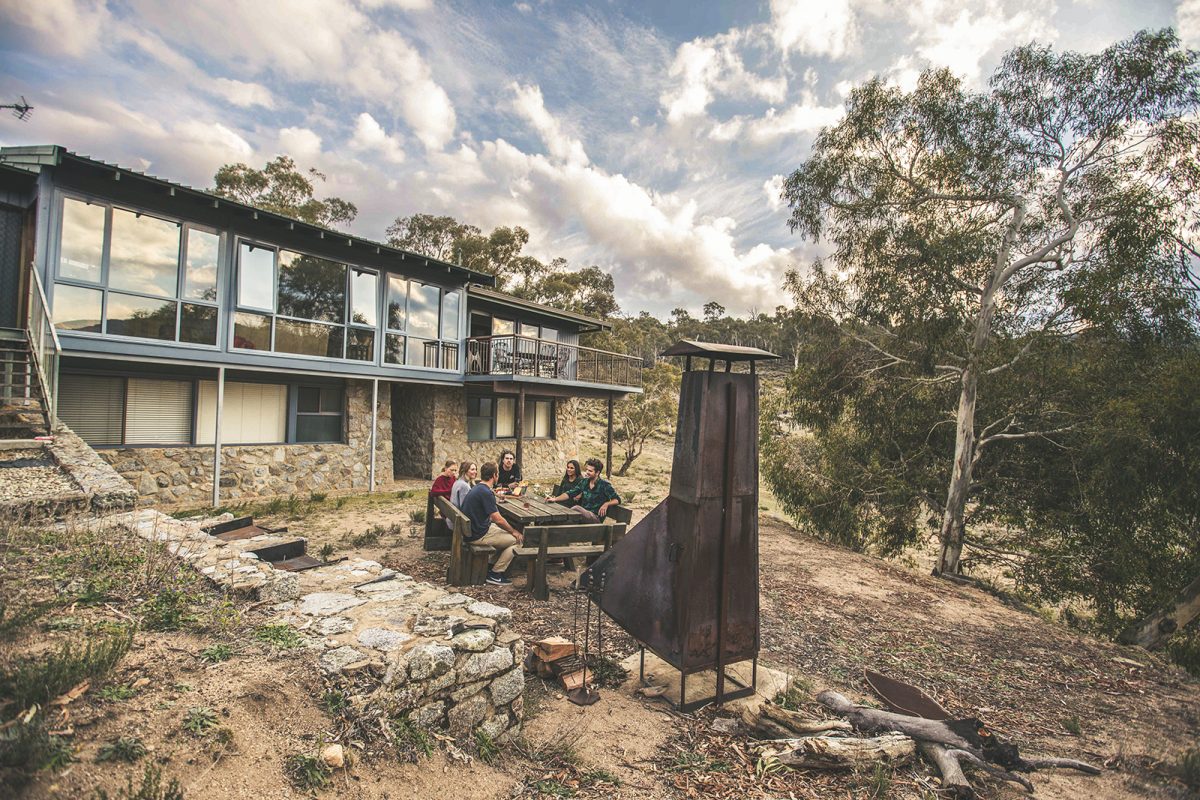 A group of people sitting outside near the outdoor fireplace at Creel Lodge, Thredbo-Perisher area in Kosciuszko National Park. Photo: Boen Ferguson/DPIE