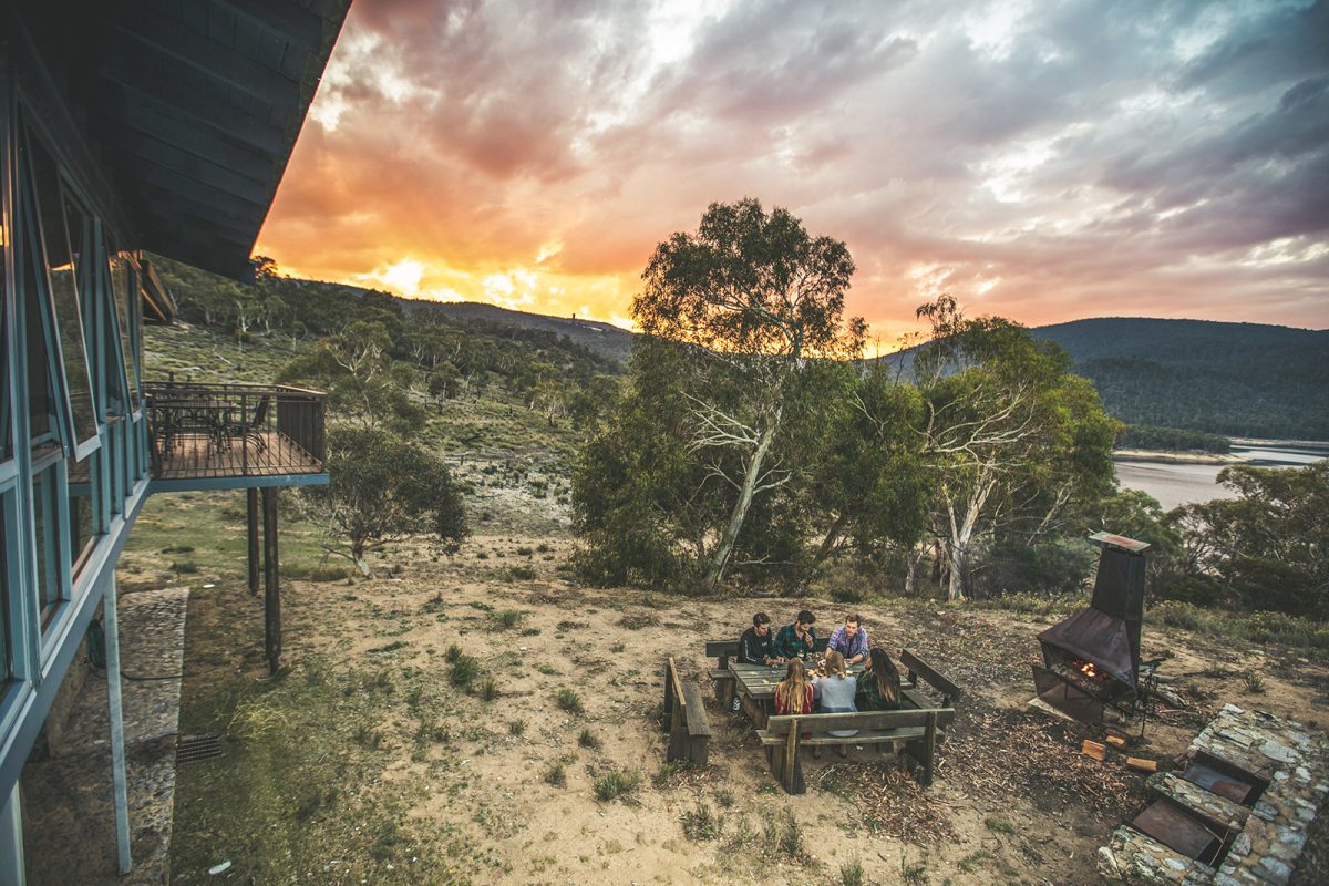 A group of people sitting outside near the outdoor fireplace at sunset at Creel Lodge, Thredbo-Perisher area in Kosciuszko National Park. Photo: Boen Ferguson/DPIE