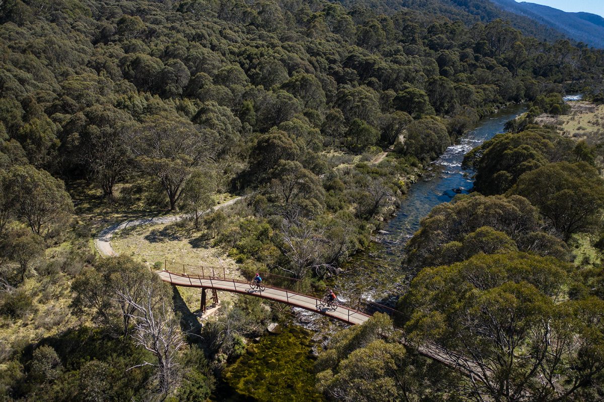Aerial view of two people riding across a suspension bridge on the Thredbo Valley track. Photo: Rob Mulally/DPIE