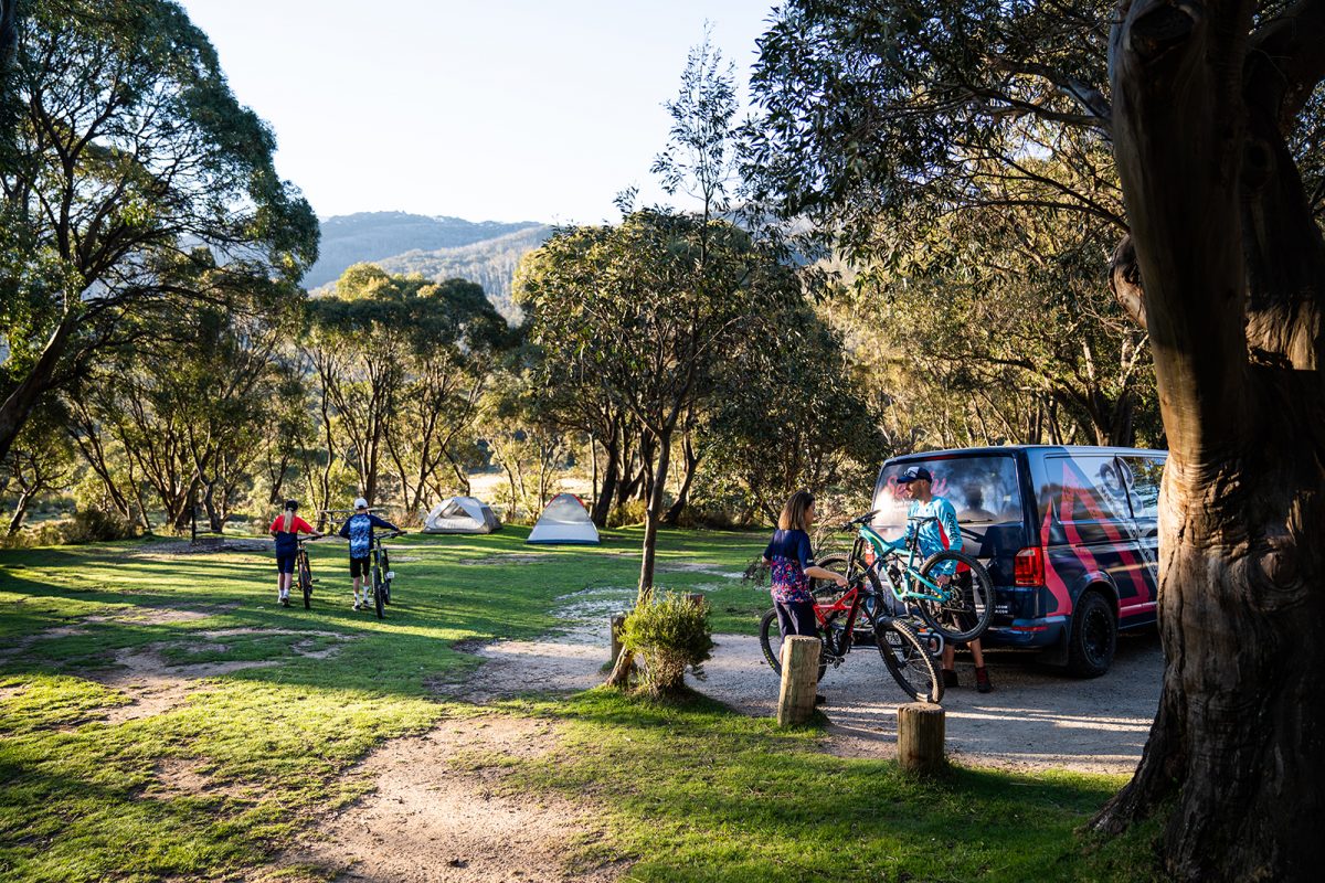 Four people walking their bikes to their tents in Thredbo Diggings campground, Thredbo-Perisher area in Kosciuszko National Park. Photo: Rob Mulally/DPIE