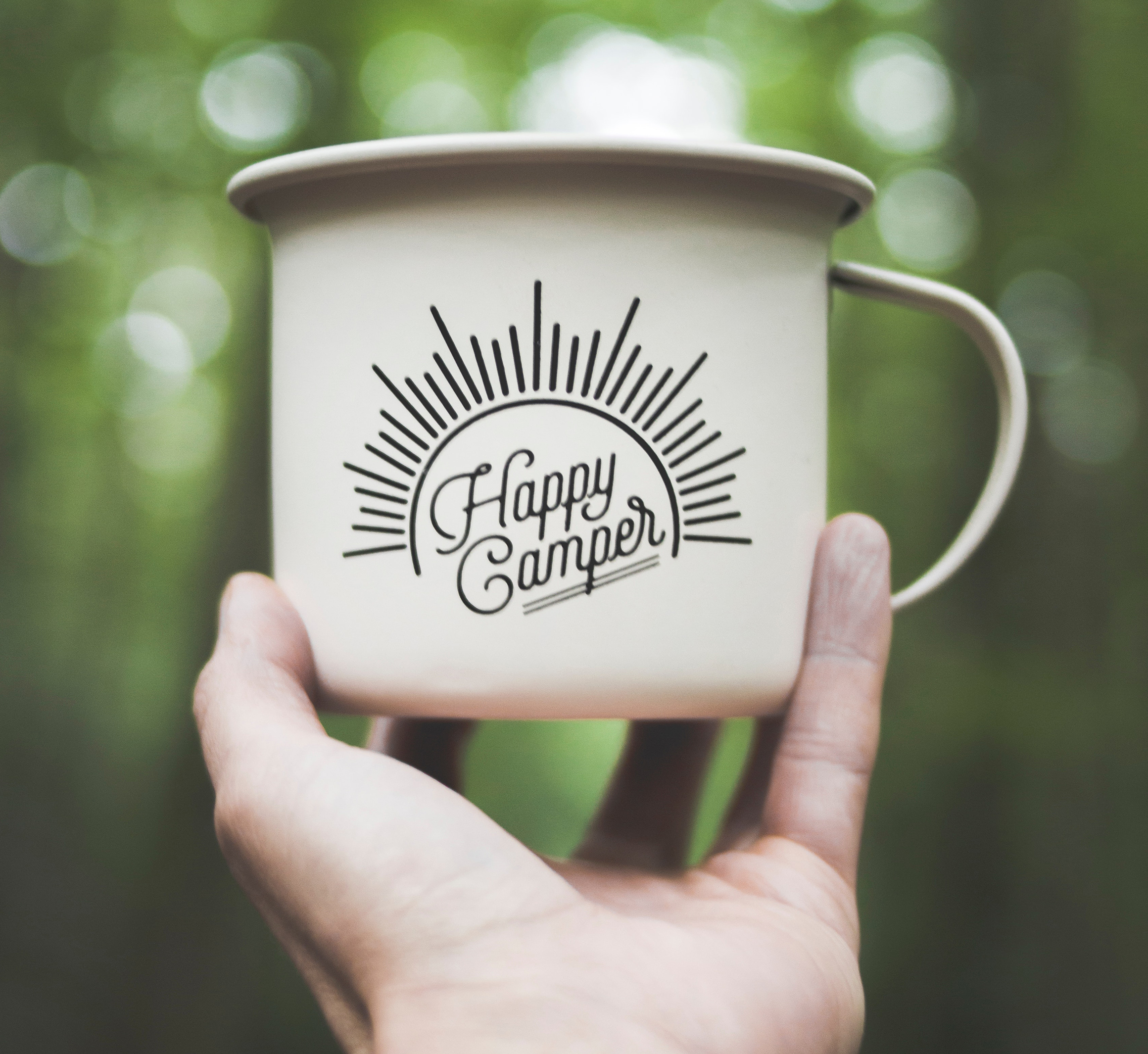 A hand holding an enamel camping cup with the writing Happy Camper. Photo: Dominika Roseclay via Pexels