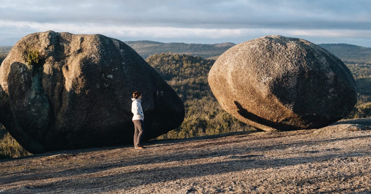 A person standing next to boulder on top of Bald Rock summit for sunrise, Bald Rock National Park. Photo credit: Harrison Candlin / DPE