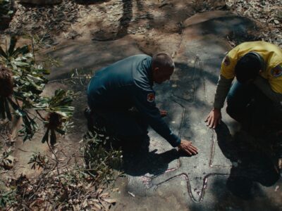 Two NPWS rangers looking at Aboriginal engravings in Ku-ring-gai Chase National Park. Photo credit: Aristo Risi/DCCEEW