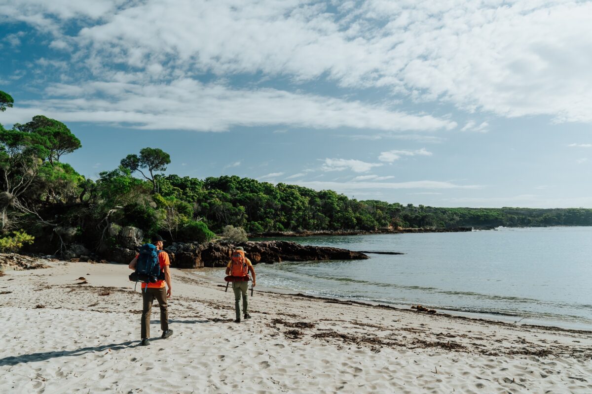 Two walkers on the sand at Bittangabee Bay on the Light to Light Walk. Photo credit: Remy Brand/DCCEEW