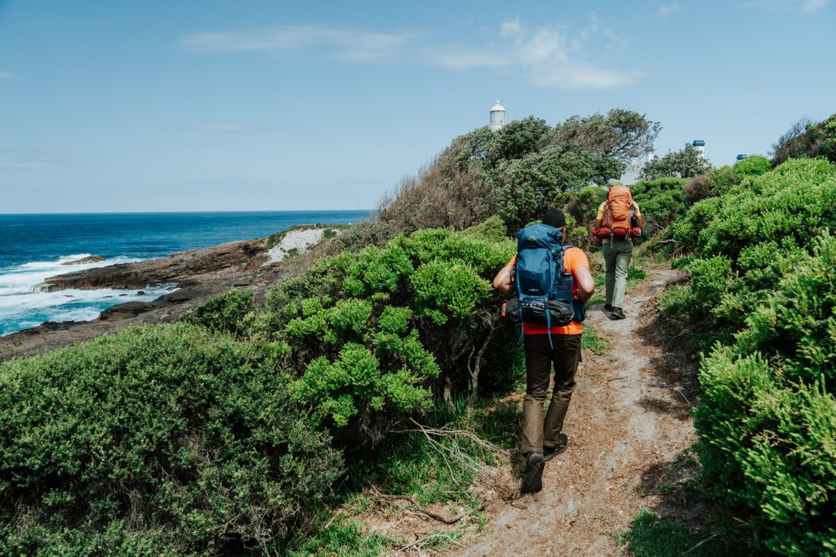 Two walkers approach Green Cape Lighthouse on the Light to Light Walk. Photo credit: Remy Brand/DCCEEW