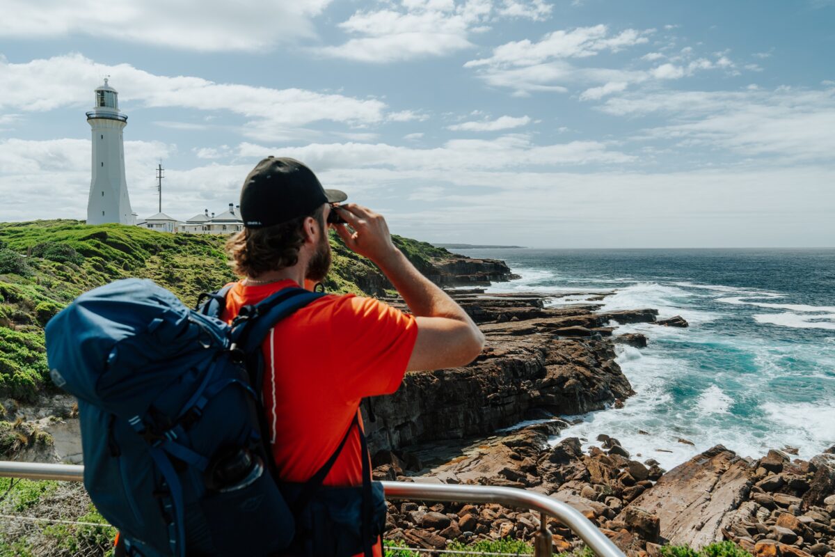 Walker looks through binoculars from the lookout at Green Cape Lighthouse on the Light to Light Walk. Photo credit: Remy Brand/DCCEEW