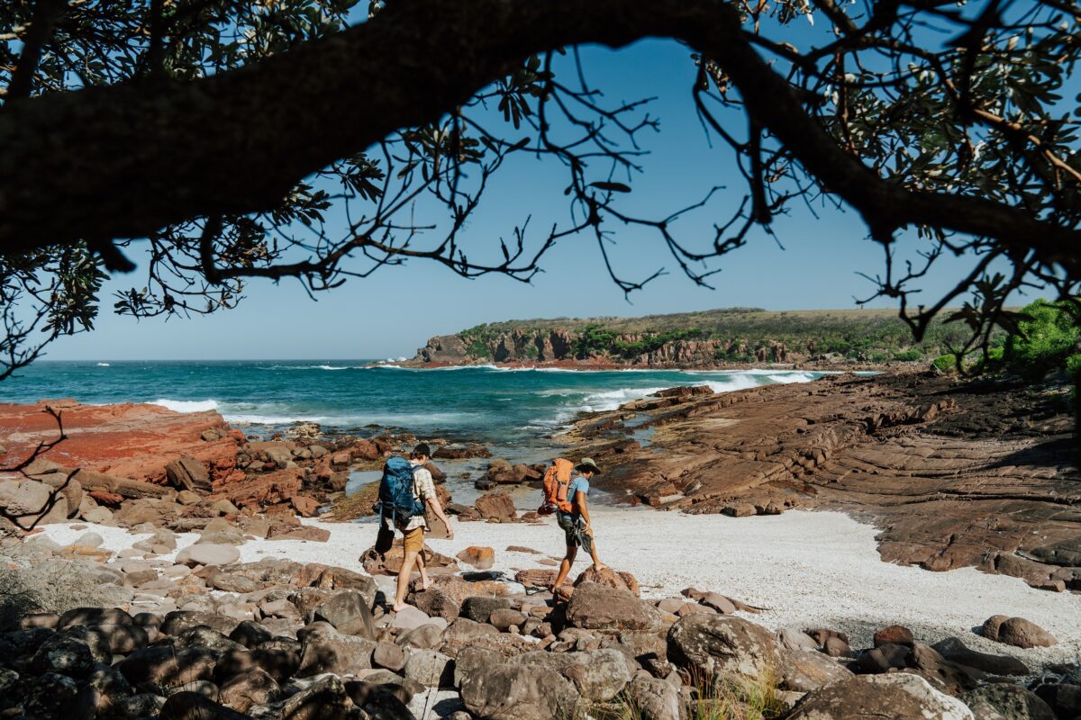 Two walkers cross the rocks at Hegartys Bay on the Light to Light Walk. Photo credit: Remy Brand/DCCEEW