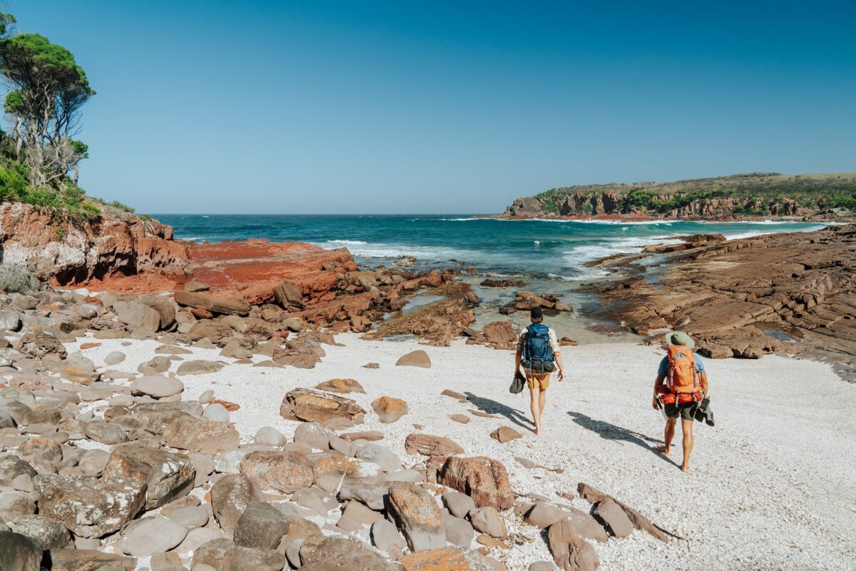 Two walkers on the sand at Hegartys Bay on the Light to Light Walk. Photo credit: Remy Brand/DCCEEW