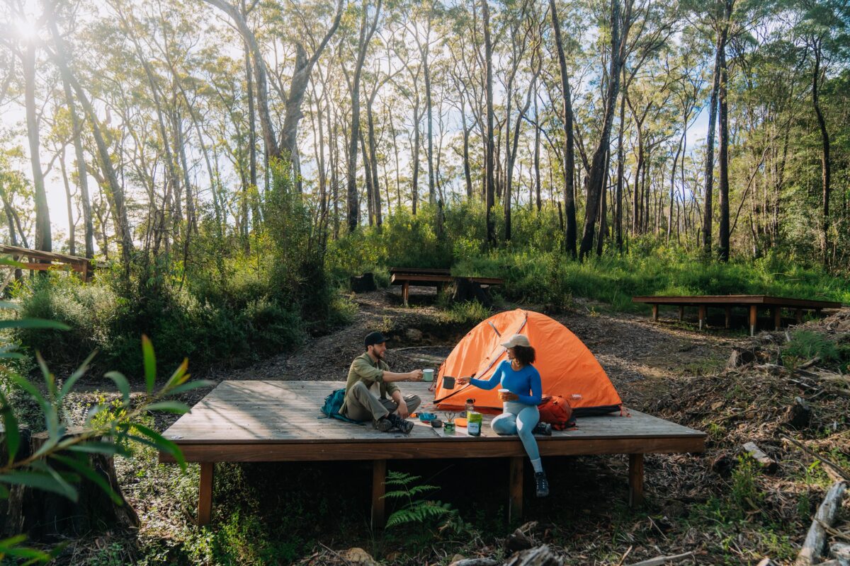 Two walkers enjoy a hot beverage on a camping platform at Yelgun Kyoomgun campground on Gidjuum Gulganyi Walk.
