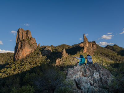 Two people sitting at enjoying the viiew from Breadknife and Grand High Tops Walk. Warrumbungles National Park. Photo credit: Rob Mulally / DCCEEW