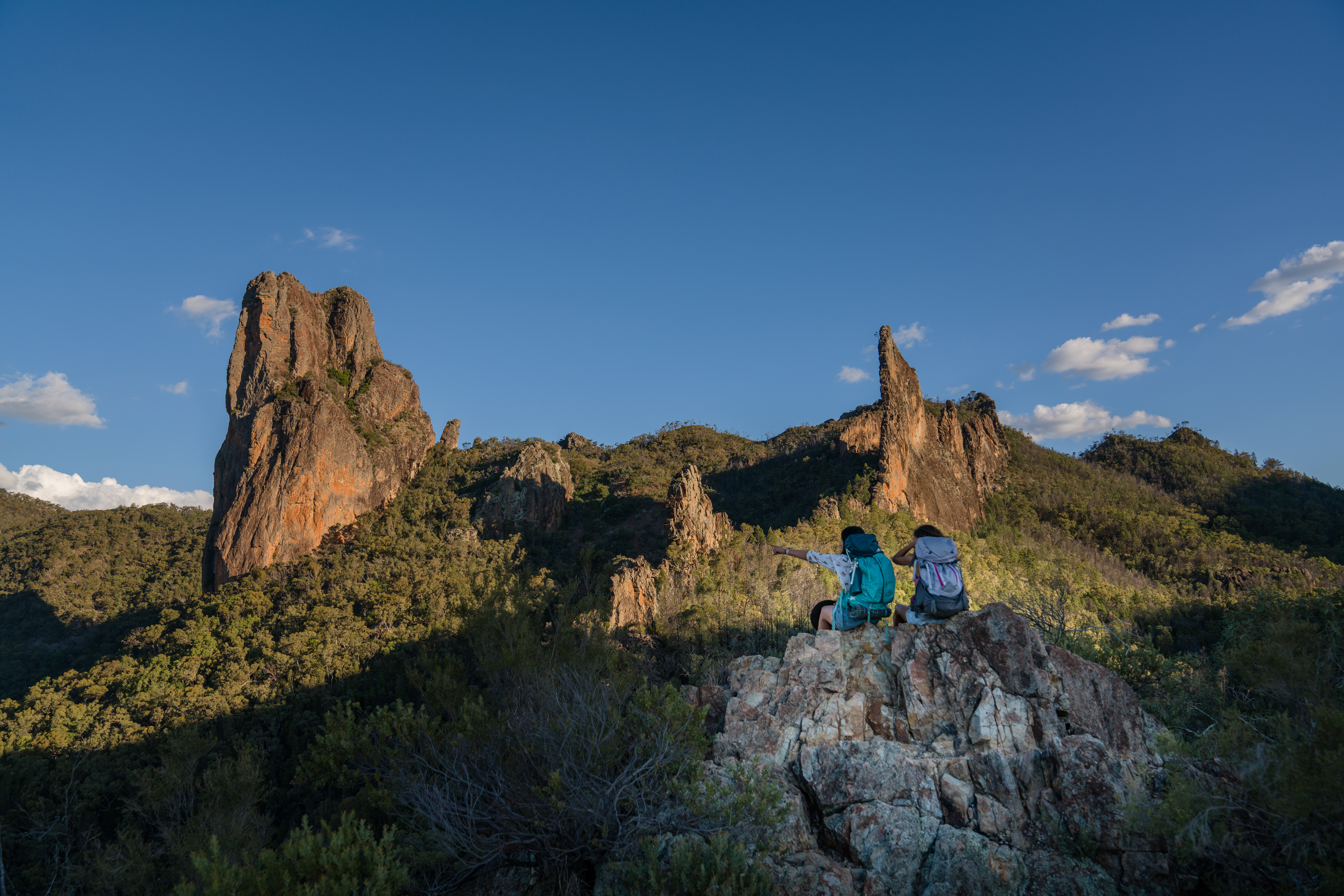Two people sitting at enjoying the viiew from Breadknife and Grand High Tops Walk. Warrumbungles National Park. Photo credit: Rob Mulally / DCCEEW